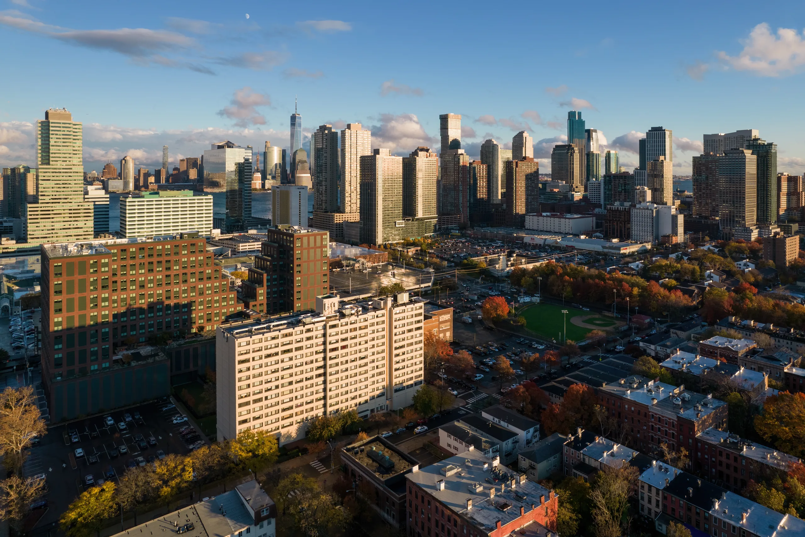 Golden-hour aerial of the Downtown Jersey City skyline rising beyond the neighborhood's parks and brick blocks