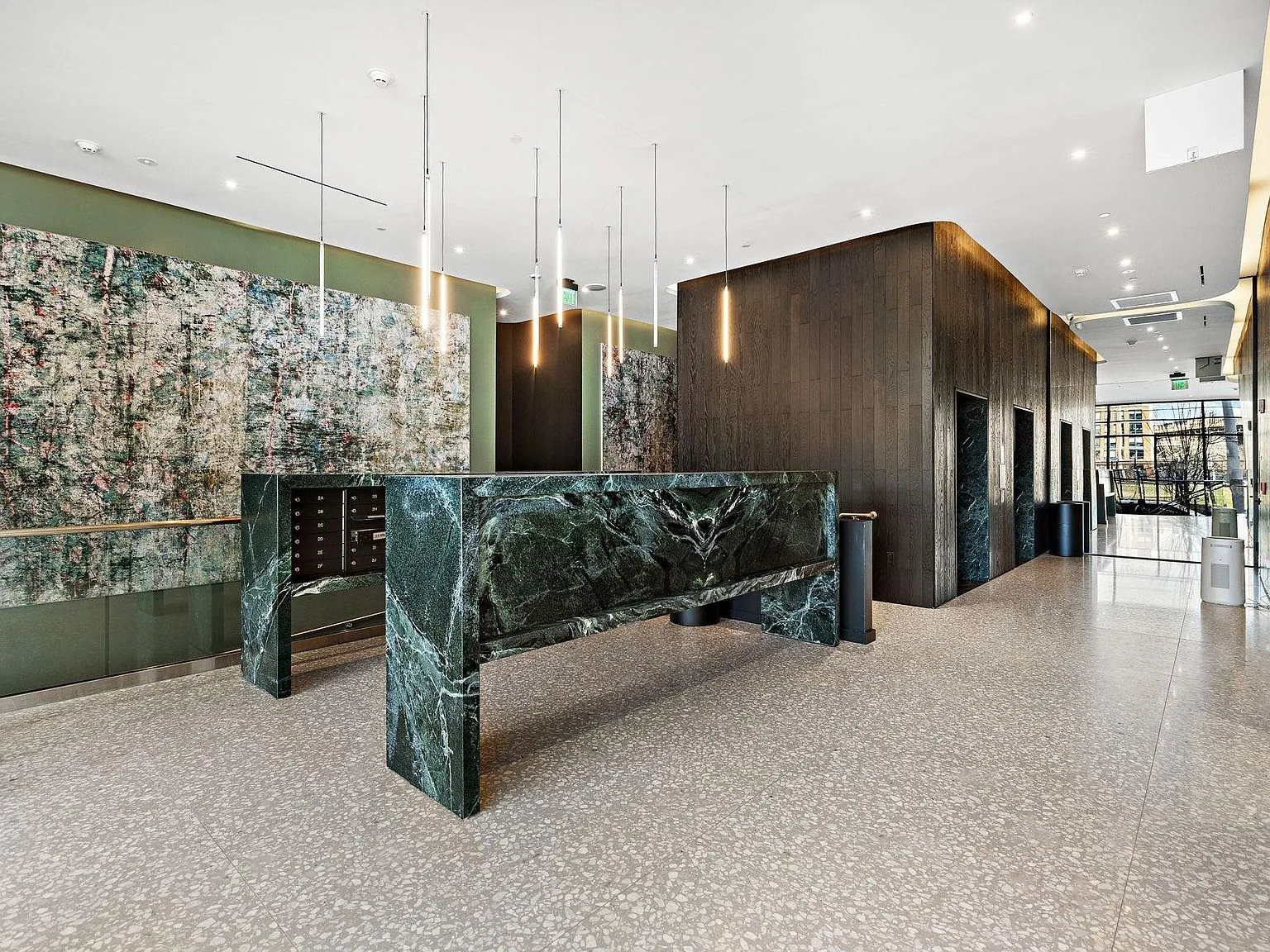 The lobby as built: verde marble console, dark-oak elevator core, and terrazzo floors